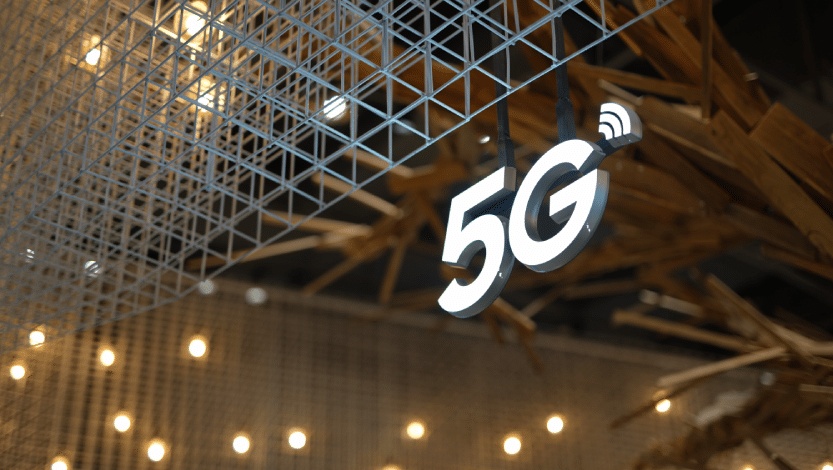 Illuminated 5G sign hanging from a modern structure, symbolizing advancements in high-speed connectivity and IoT integration.