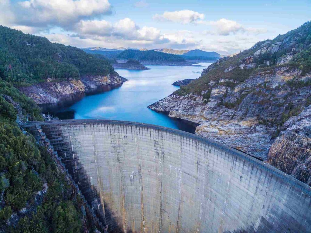 A large dam surrounded by lush mountains and a reservoir, showcasing renewable energy generation that can be optimized with IoT connectivity for real-time monitoring.