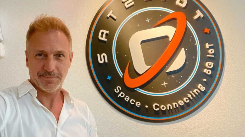Gianluca Redolfi, CCO of Sateliot, posing confidently with the Sateliot logo displayed prominently in the background. IoT connectivity underscores Sateliot's mission to provide seamless global communication through satellite technology.
