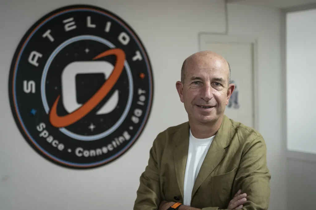 Jaume Sanpera posing confidently for a photo with Sateliot's logo displayed prominently in the background. IoT connectivity represents Sateliot's innovative vision of linking devices worldwide through satellite technology.