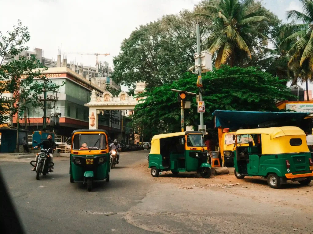 A lively street in India with yellow and green auto-rickshaws and taxis weaving through the bustling traffic. IoT connectivity enables real-time navigation and tracking, improving urban mobility and fleet management in crowded cityscapes.