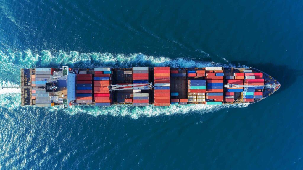 Overhead view of a container ship with IoT sensors for real-time tracking, sailing through the ocean with waves trailing behind.