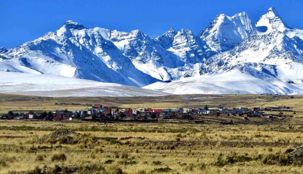 A small town nestled in the Andes Mountains, with snowy peaks towering above. Solar panels highlight the use of satellite IoT connectivity amidst the natural beauty.