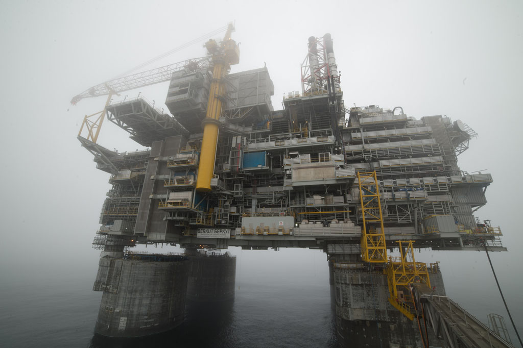 The Berkut oil rig, a massive steel platform in the icy Sea of Okhotsk, stands tall above the water, equipped with cranes, pipelines, and machinery against a backdrop of cold, remote ocean.